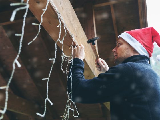 Man met kerstmuts hangt sierverlichting op aan schuur