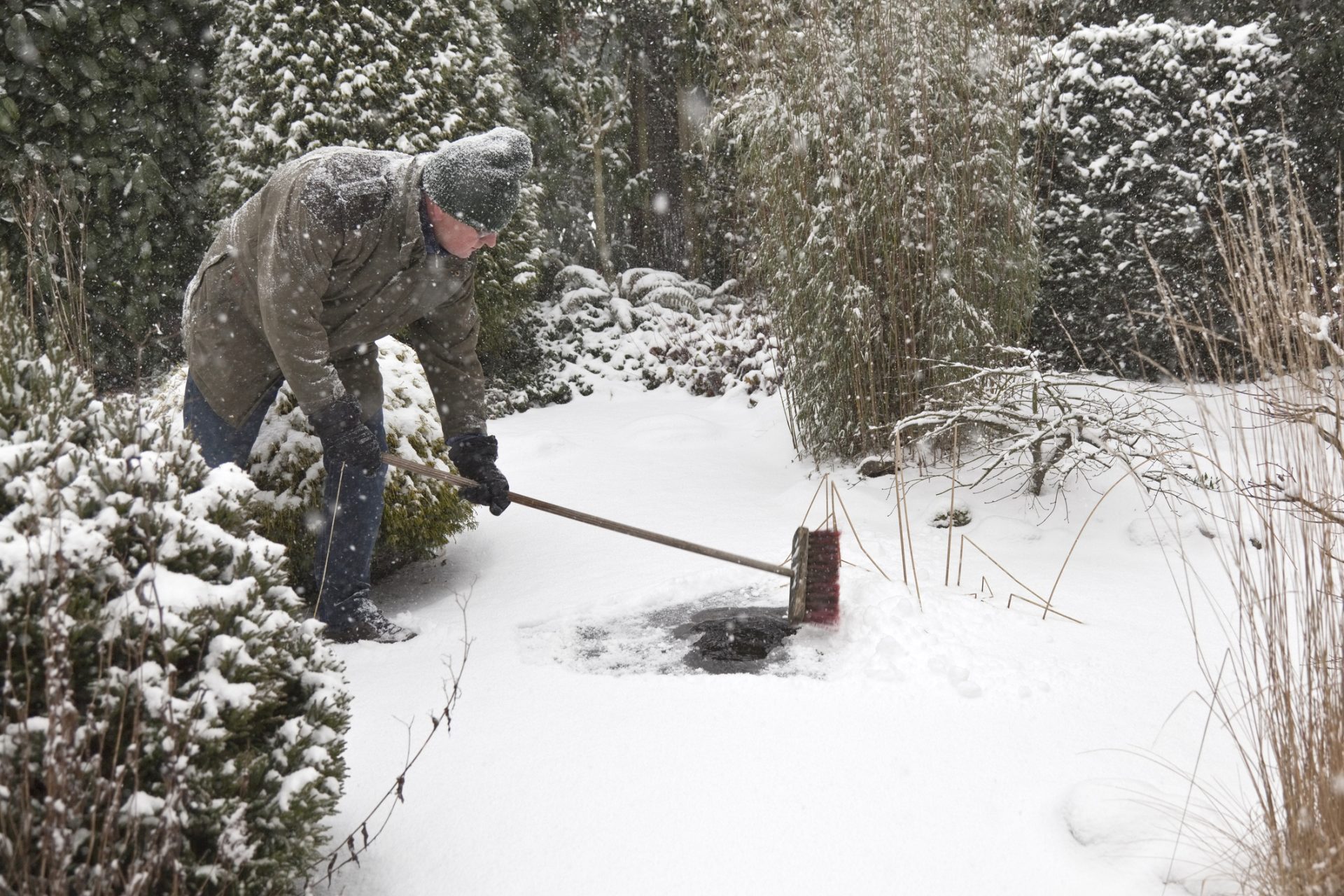 Man veegt sneeuw van bevroren vijver af in de winter