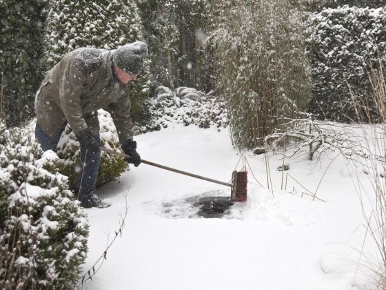 Man veegt sneeuw van bevroren vijver af in de winter